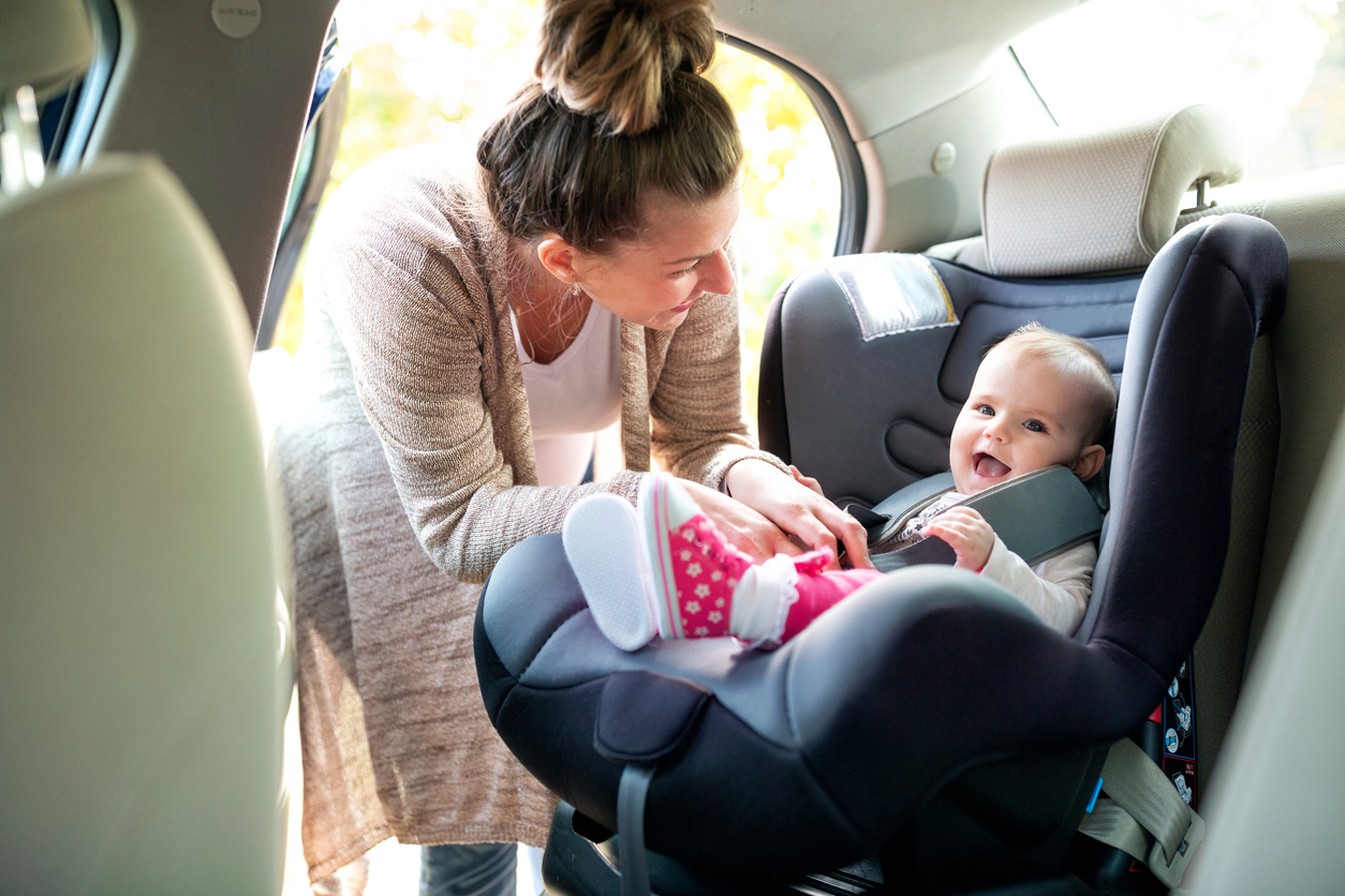Mother securing toddler in a car seat.