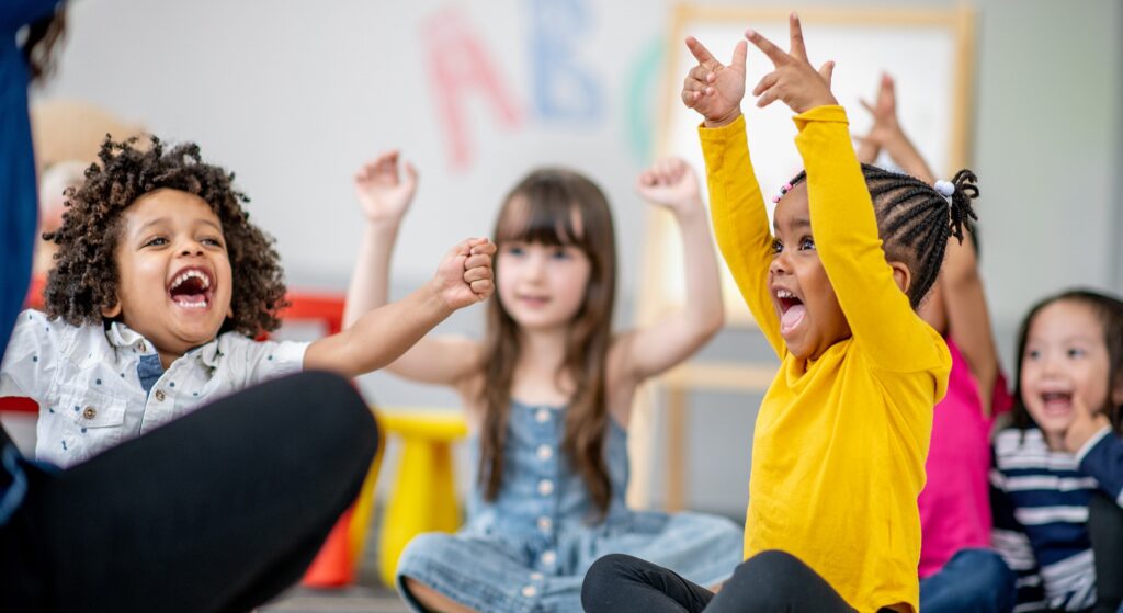 Preschool students with hands up playing a game at school