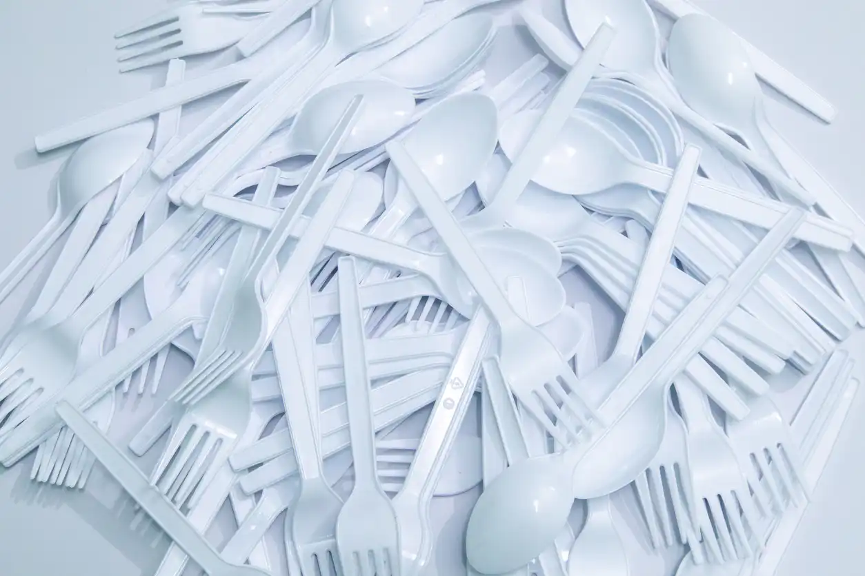 White plastic forks, spoons, and knives stacked together, representing fast food culture and takeaway convenience. Great for illustrating environmental impact of single-use plastics, food packaging trends, and sustainability topics in editorials or commercial use.
